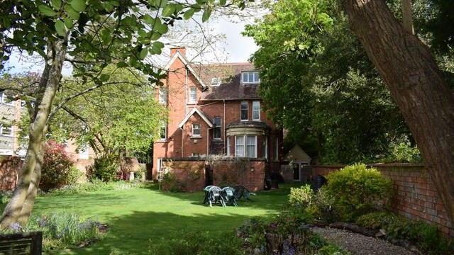 The rear features of a Victorian brick-built house with a large garden to the foreground